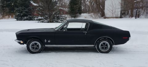 1968 Ford Mustang - A black coupe sits in a snowy landscape, its body style suggesting a late 1960s model.