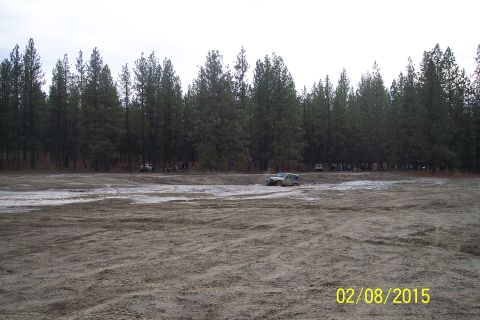 1990 Ford Bronco - An SUV is stuck in the mud with other vehicles and trees visible in the distance.