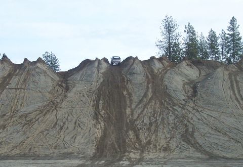 1990 Ford Bronco - An SUV navigates a challenging ascent up a large dirt mound, leaving visible tire tracks on the terrain.