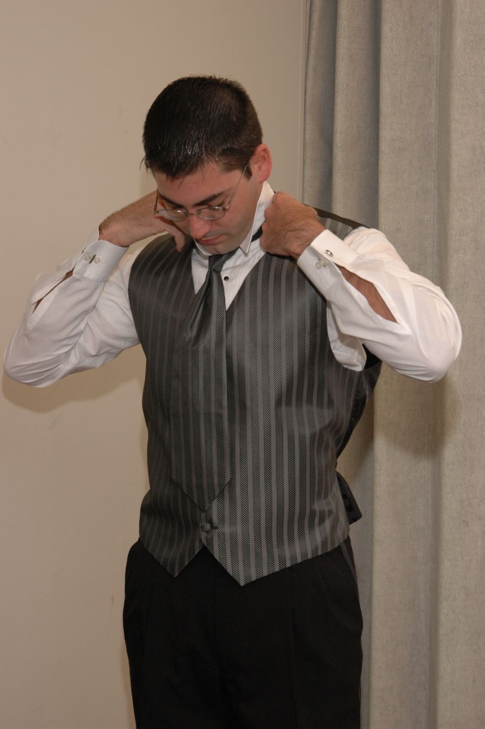 Man in a white dress shirt, grey striped vest, and black pants adjusting his tie