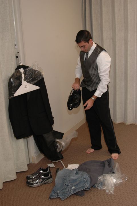 1985 Ford Crown Victoria LTD - A man prepares for a wedding, holding dress shoes while a suit hangs nearby and casual clothes are on the floor.