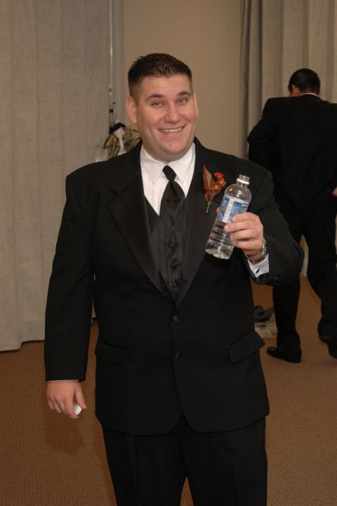 1985 Ford Crown Victoria LTD - A man in formal wear smiles while holding a bottle of water, with another person in a suit visible in the background.