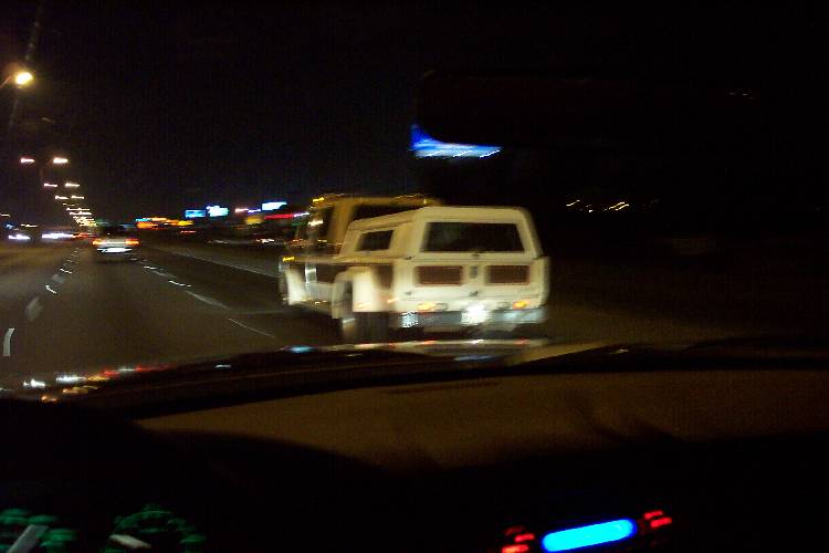 Blurry night highway view from a car following a white truck with camper shell