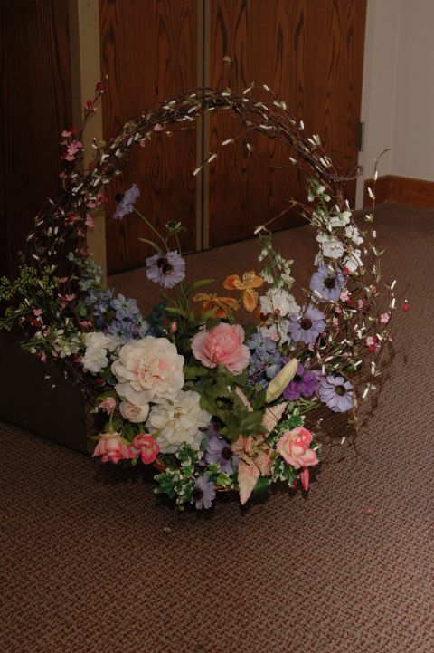 1985 Ford Crown Victoria LTD - A decorative basket filled with various artificial flowers and branches sits on a carpeted floor in front of wooden doors.