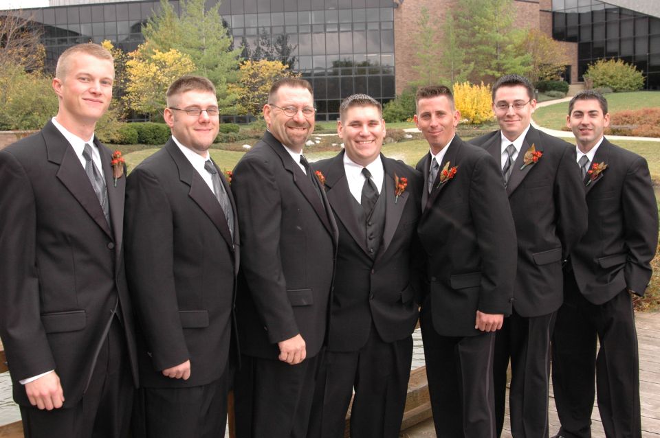 Group of men in tuxedos standing outdoors with a building in the background