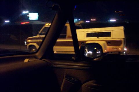 1992 Ford Bronco - A two-tone Ford pickup truck with a camper shell is seen from inside another vehicle at night.
