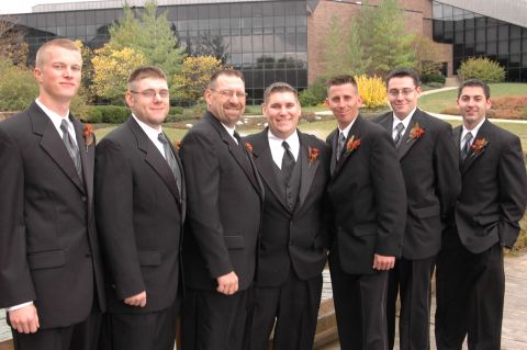 1985 Ford Crown Victoria LTD - A wedding party poses for a photo outdoors in front of a modern building with autumn foliage.