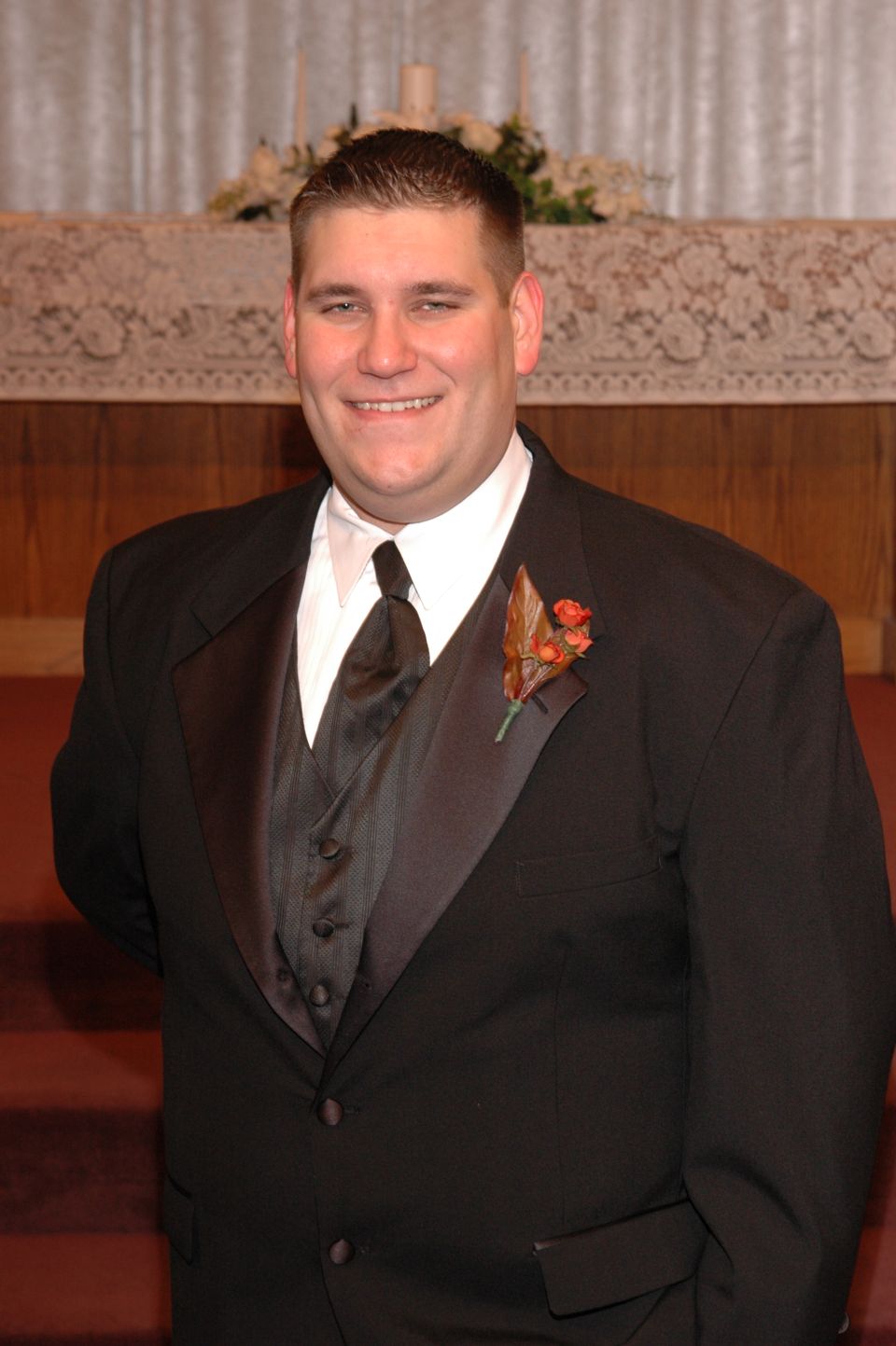 Man in a black tuxedo with a white shirt and black tie, wearing a boutonniere
