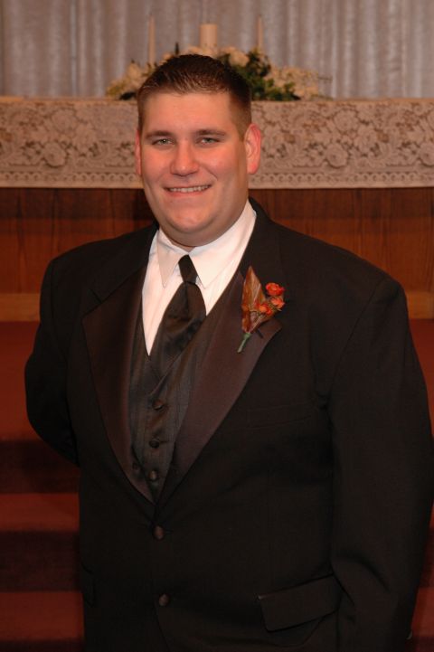 1985 Ford Crown Victoria LTD - A groom smiles for a photo in a tuxedo, standing in front of an altar.