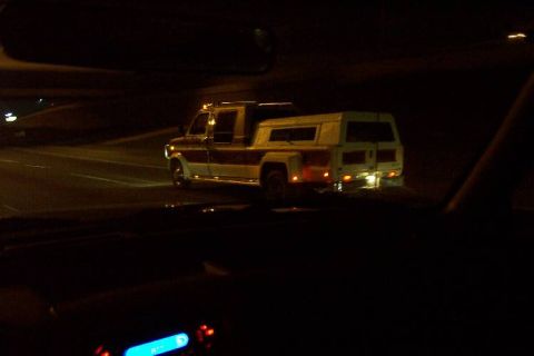 1992 Ford Bronco - A custom pickup truck with a camper shell drives down a road at night.