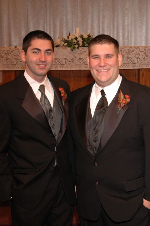 1985 Ford Crown Victoria LTD - Two men dressed in formal wedding attire pose for a photograph in front of a decorative altar cloth.