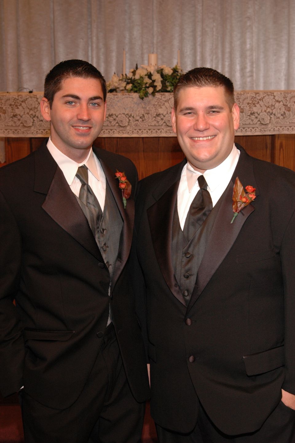 two men in black tuxedos with grey vests and ties stand side-by-side