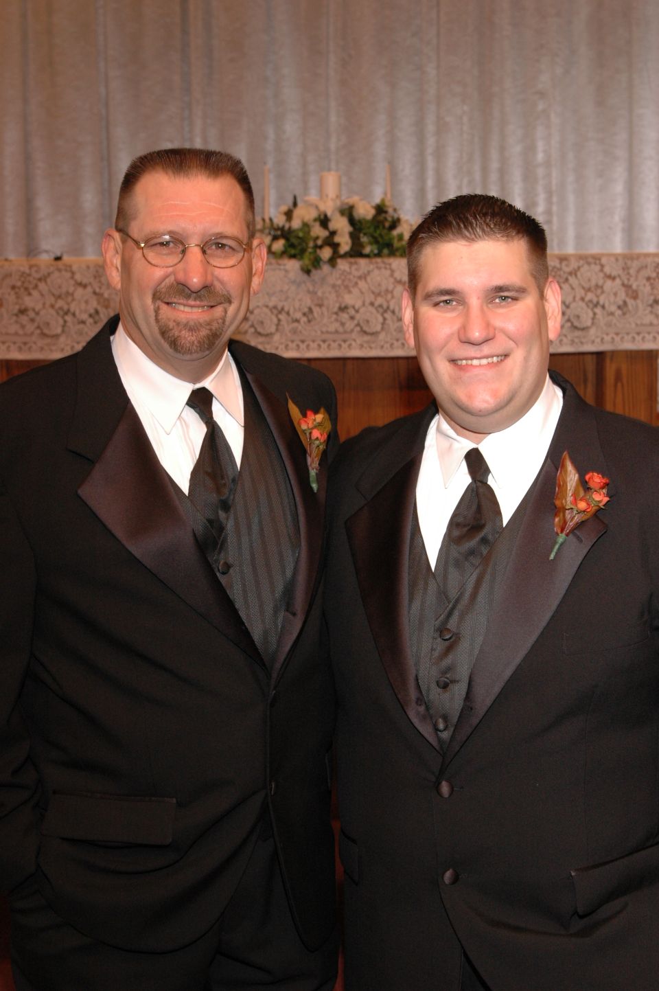 Two men in formal wear, one older with glasses and a goatee, the other younger, both smiling