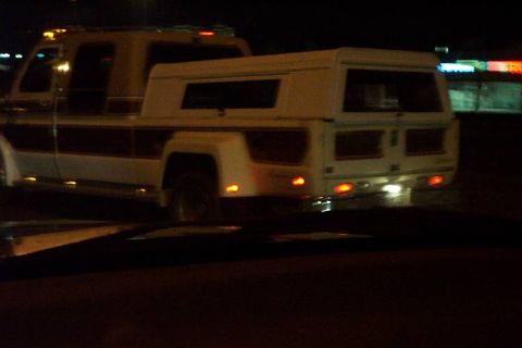 1992 Ford Bronco - This custom pickup truck features a camper shell and dual rear wheels, seen from the back at night.