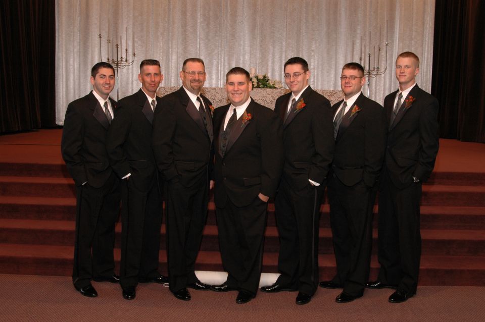 Group of seven men in black tuxedos standing on steps