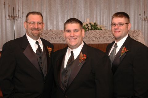 1985 Ford Crown Victoria LTD - Three men dressed in formal wear pose for a photograph, likely at a wedding event.