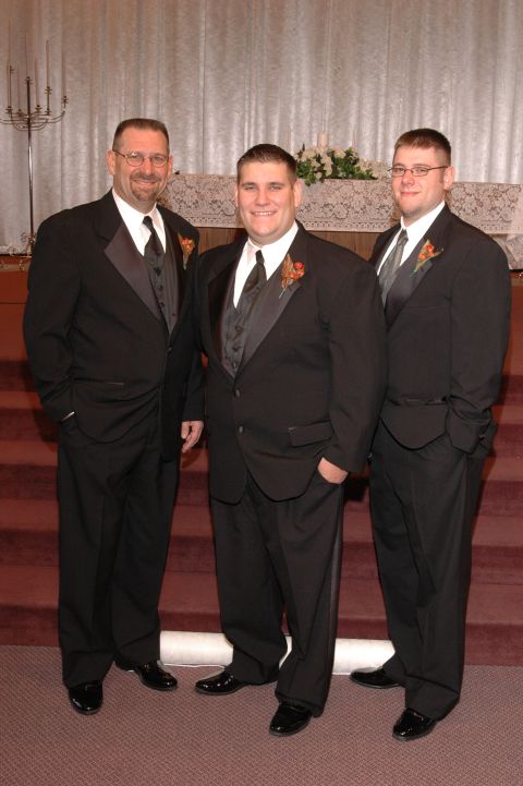 1985 Ford Crown Victoria LTD - Three men in formal wear pose for a photograph in what appears to be a wedding venue.