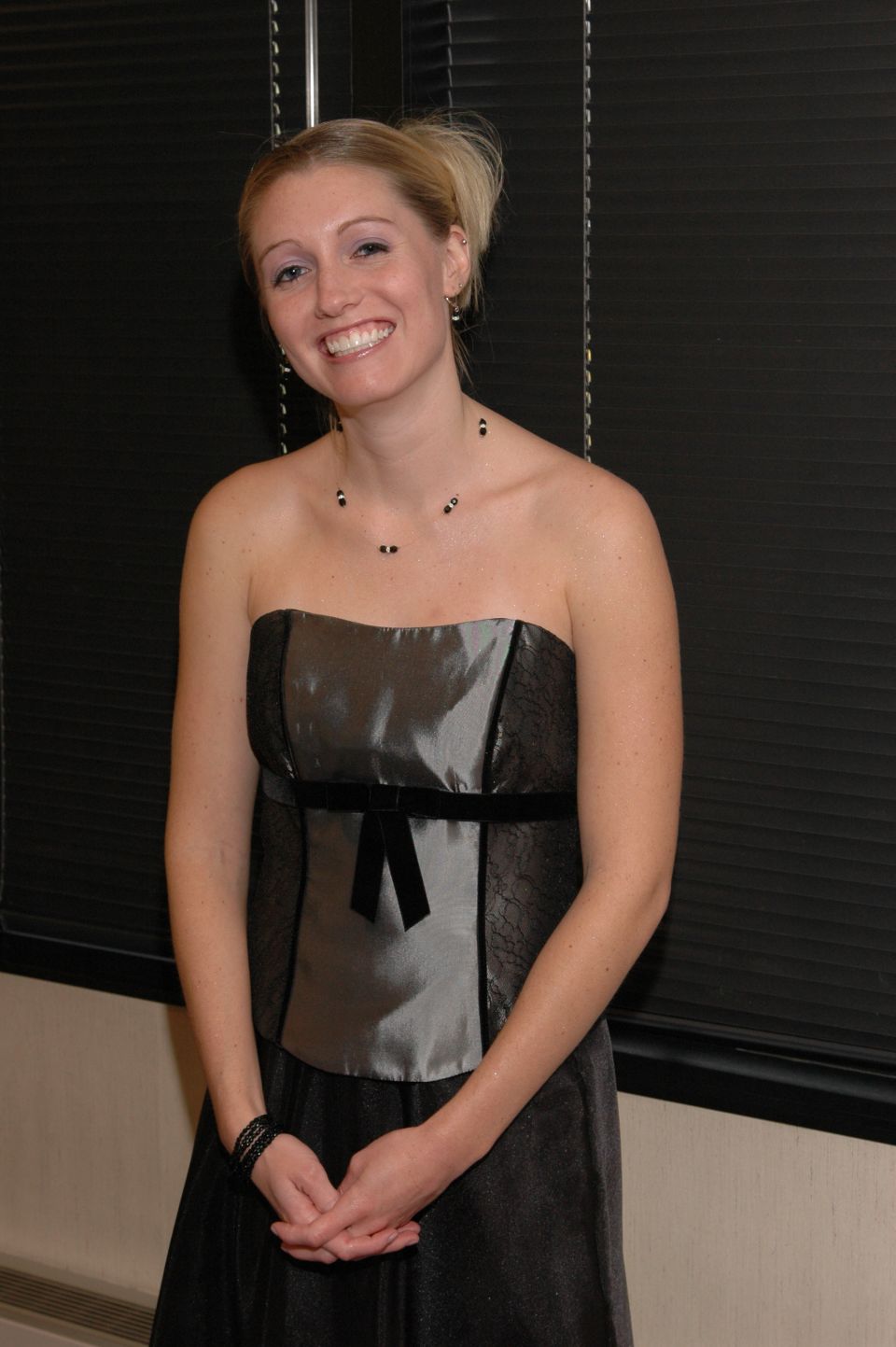 Woman in a strapless grey and black formal dress with her hands clasped in front of her