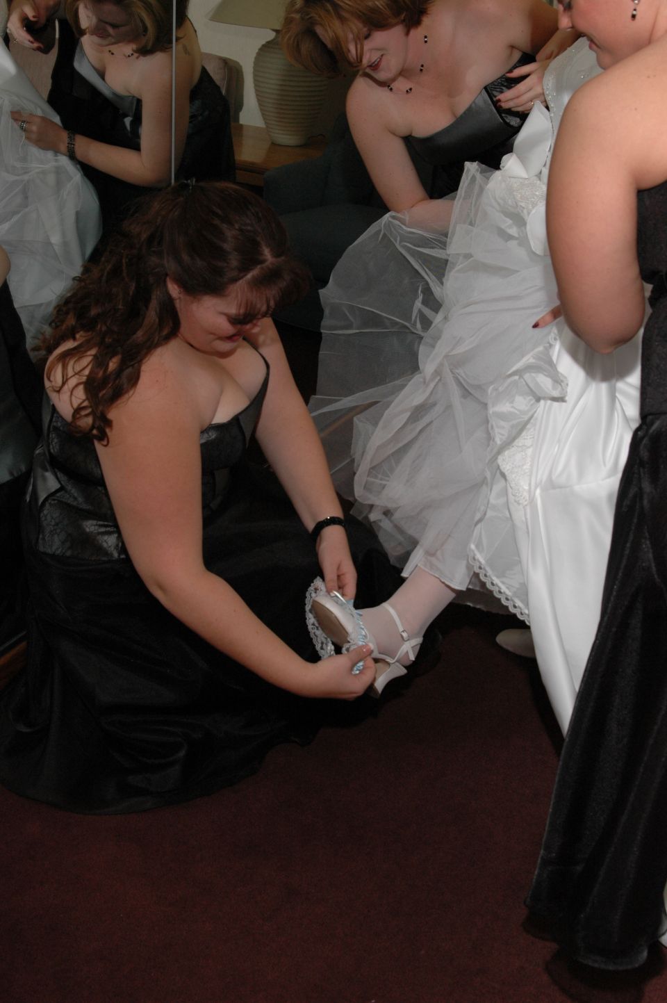 Woman in black dress fastens shoe on bride's foot