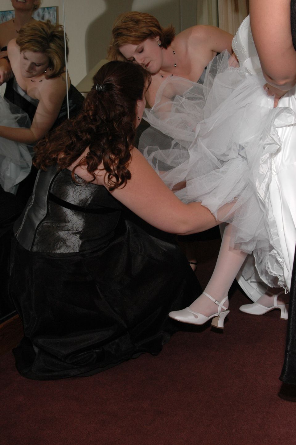 Women adjusting a wedding dress, one is kneeling