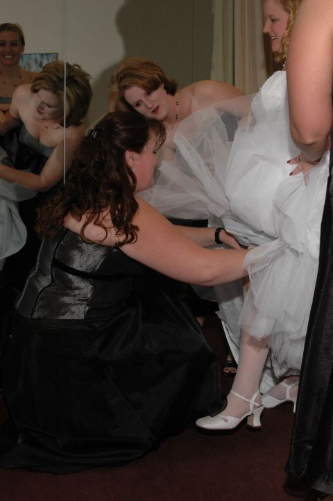 1985 Ford Crown Victoria LTD - Several women are gathered around, helping to adjust a wedding dress in what appears to be a bridal shop or dressing room.