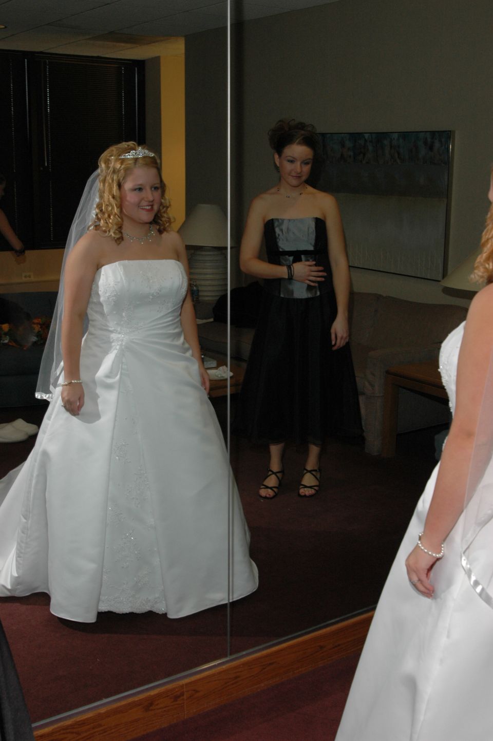 Bride in white wedding dress and bridesmaid in black dress reflected in a mirror