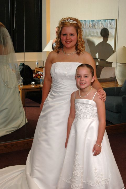 1985 Ford Crown Victoria LTD - A bride and a flower girl pose for a photo in their wedding attire, with reflections visible in a large mirror behind them.