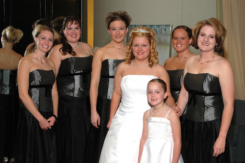 Wedding party with bride in white dress and bridesmaids in black dresses, standing indoors