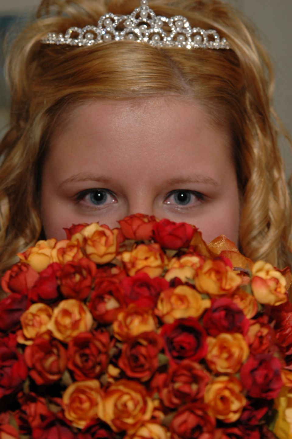 Bride's eyes peek over a bouquet of red and orange roses, wearing a tiara