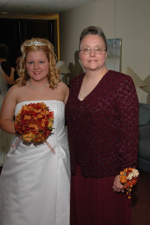 1985 Ford Crown Victoria LTD - A bride in a white dress and her mother in a burgundy dress pose together at a wedding event.