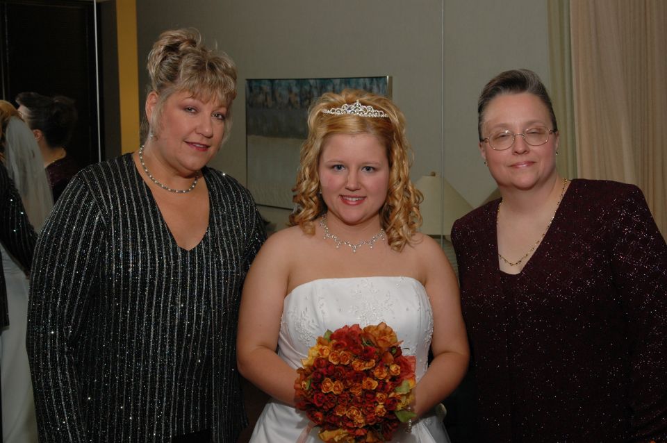 Bride with two women, one on each side. Bride holds a bouquet