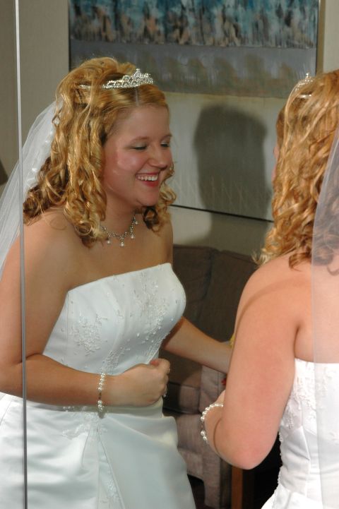 1985 Ford Crown Victoria LTD - A bride in a white wedding dress and tiara smiles as she looks at her reflection in a mirror.