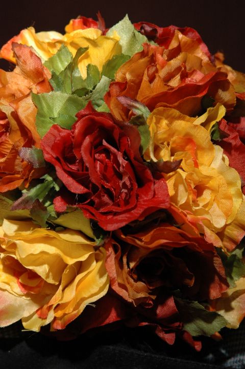 1985 Ford Crown Victoria LTD - A close-up view of a bouquet artificial flowers in autumnal colors, including red, orange, and yellow roses with green leaves.