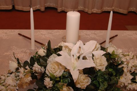 1985 Ford Crown Victoria LTD - A wedding scene a central pillar candle flanked by two taper candles amidst a white floral arrangement.