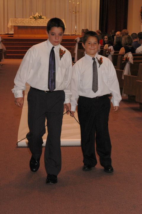 1985 Ford Crown Victoria LTD - Two boys in formal attire walk down an aisle, holding a rope connected to a rolled-up carpet.