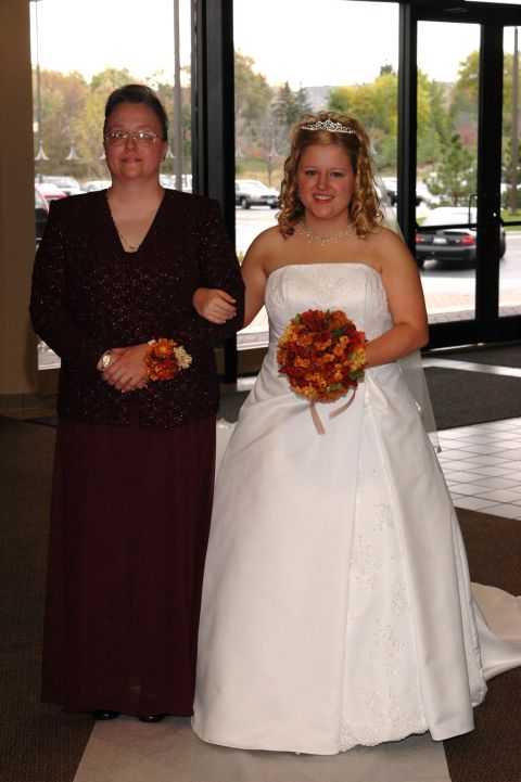 1985 Ford Crown Victoria LTD - A bride and her mother pose for a photo indoors, with cars visible through the glass doors behind them.