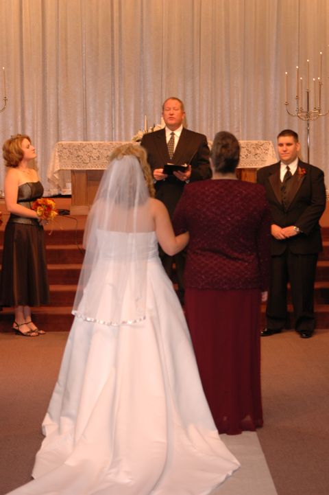 1985 Ford Crown Victoria LTD - A wedding ceremony is taking place with the bride and groom at the altar, surrounded by their wedding party and an officiant.
