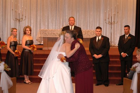 1985 Ford Crown Victoria LTD - A bride is embraced by a woman during a wedding ceremony, with wedding party members standing nearby.
