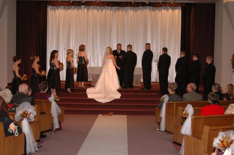 1985 Ford Crown Victoria LTD - A wedding ceremony takes place in a chapel with the wedding party standing at the altar and guests seated in pews.