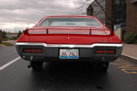1985 Ford Crown Victoria LTD - Rear view of a red car with a spoiler and dual exhaust pipes, parked in a lot.
