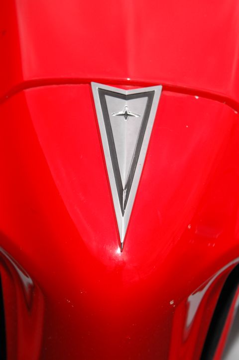 1985 Ford Crown Victoria LTD - Close-up of a red car's hood showing a silver emblem with a bird design.