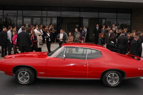 1985 Ford Crown Victoria LTD - A red 1967 Pontiac GTO is parked outside a building while a group of people stand nearby.