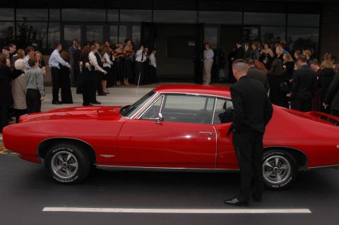 1985 Ford Crown Victoria LTD - A red 1967 Pontiac GTO coupe is parked outside a building with people gathered.