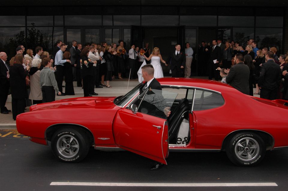 red vintage coupe with driver's door open, wedding party in background