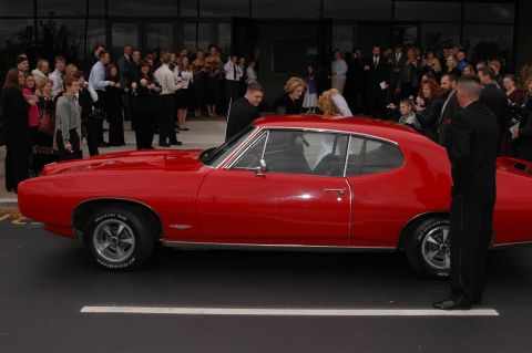 1985 Ford Crown Victoria LTD - A red 1960s coupe is the centerpiece of a gathering, possibly for a wedding event.