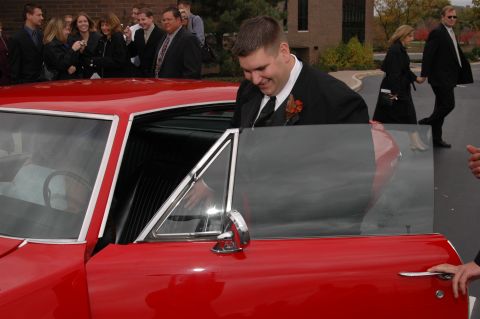 1985 Ford Crown Victoria LTD - A man in a tuxedo exits a red coupe, with wedding guests in the background.