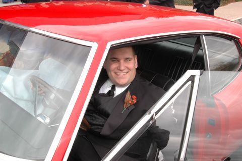1985 Ford Crown Victoria LTD - Man in formal wear sits in the driver's seat of a classic red automobile.