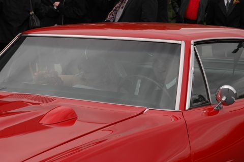 1985 Ford Crown Victoria LTD - A red classic car is seen from the front, with people inside and onlookers in the background.