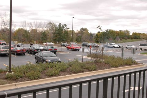 1985 Ford Crown Victoria LTD - A parking lot scene shows multiple vehicles parked and driving under a cloudy sky.