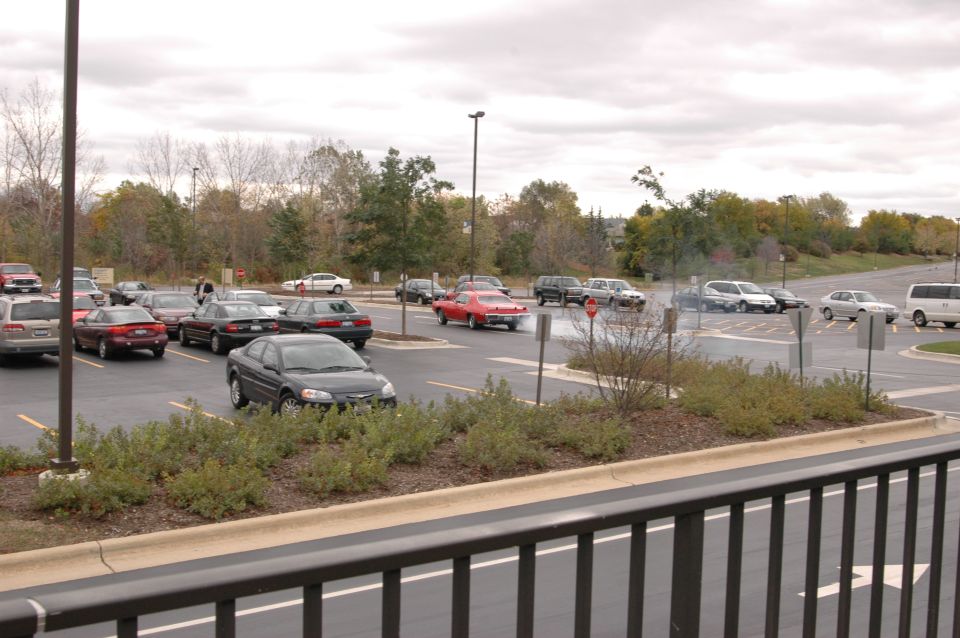 Parking lot scene with various cars, including a red coupe, under an overcast sky